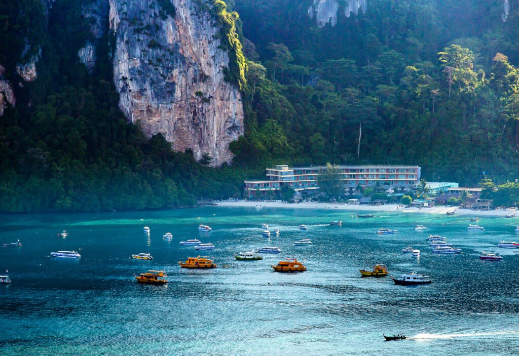 Scenic view of Thailand’s Phi Phi Island featuring turquoise water, white-sand beaches, limestone cliffs, and tropical long-tail boats.
