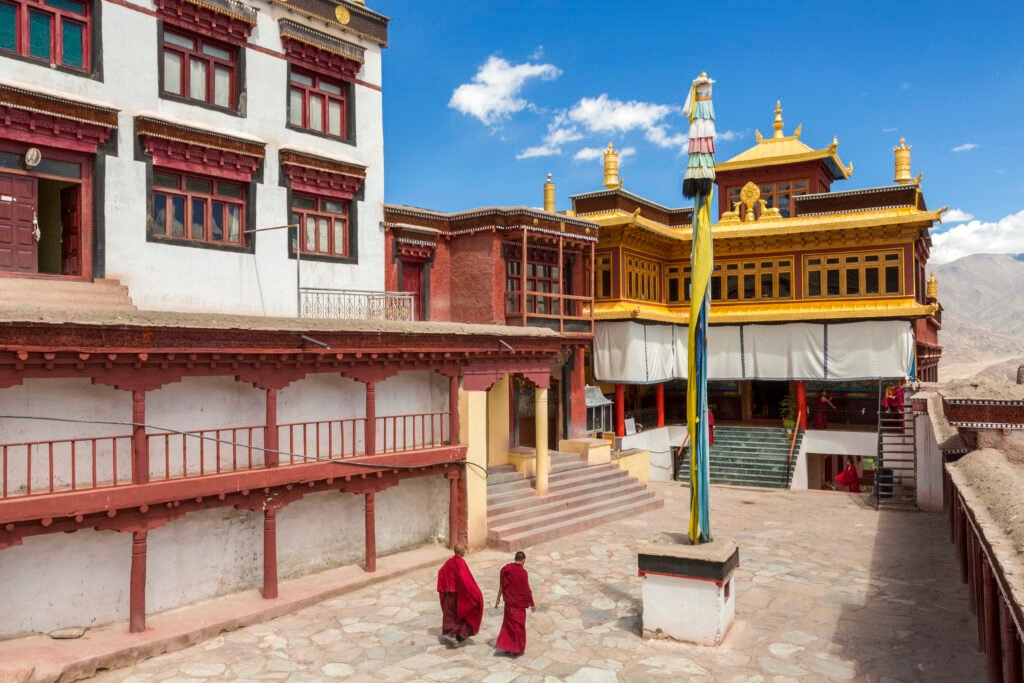 ladakh,india,exterior view of buddhist monastery with two monks walking across courtyard.