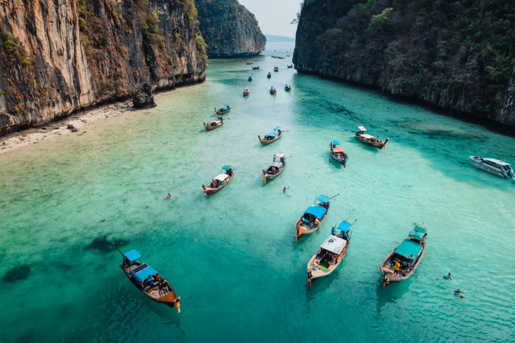 Longtail boats floating on clear turquoise waters between limestone cliffs at Phi Phi Islands, Thailand.