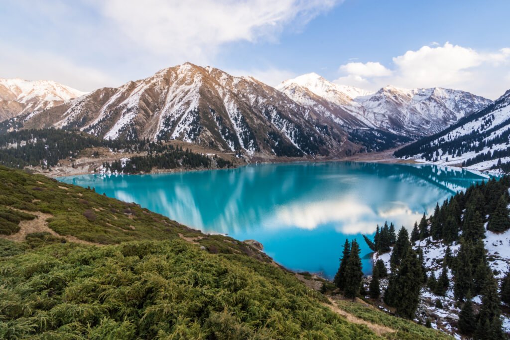 Turquoise Big Almaty Lake surrounded by snow-capped Tian Shan mountains and evergreen trees